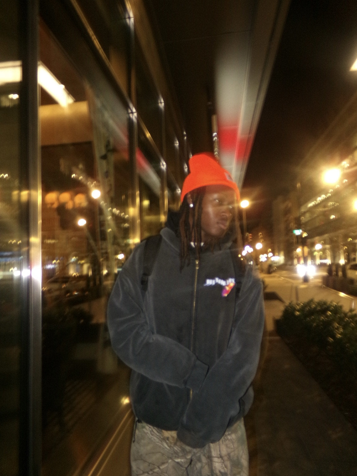 Streetwear portrait at night featuring an orange beanie and dark hoodie